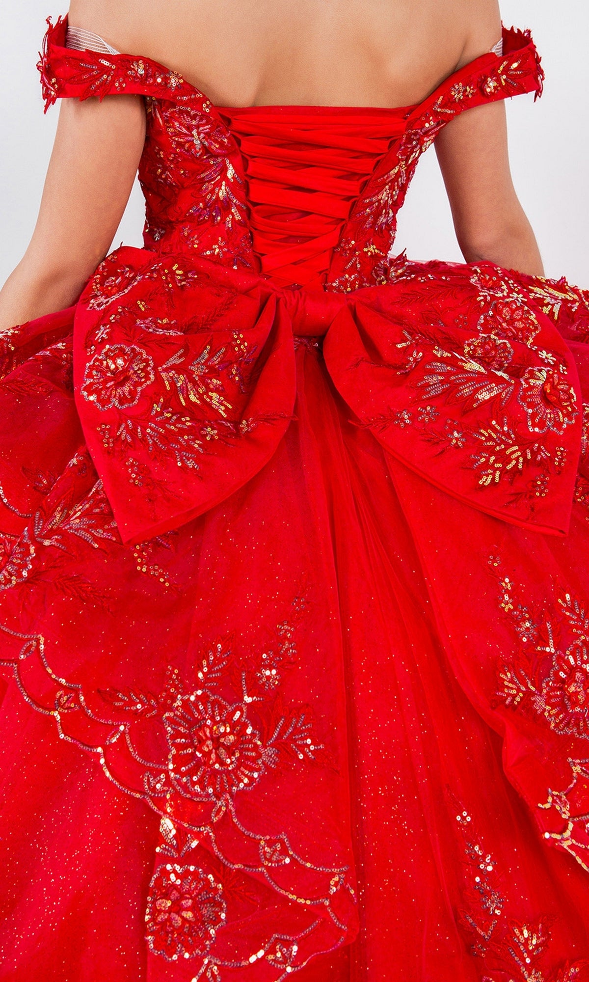 A woman wears the Quinceanera Ball Gown 8100J, featuring an off the shoulder design, lace-up back, large bow, gold floral embroidery, and iridescent beaded details.